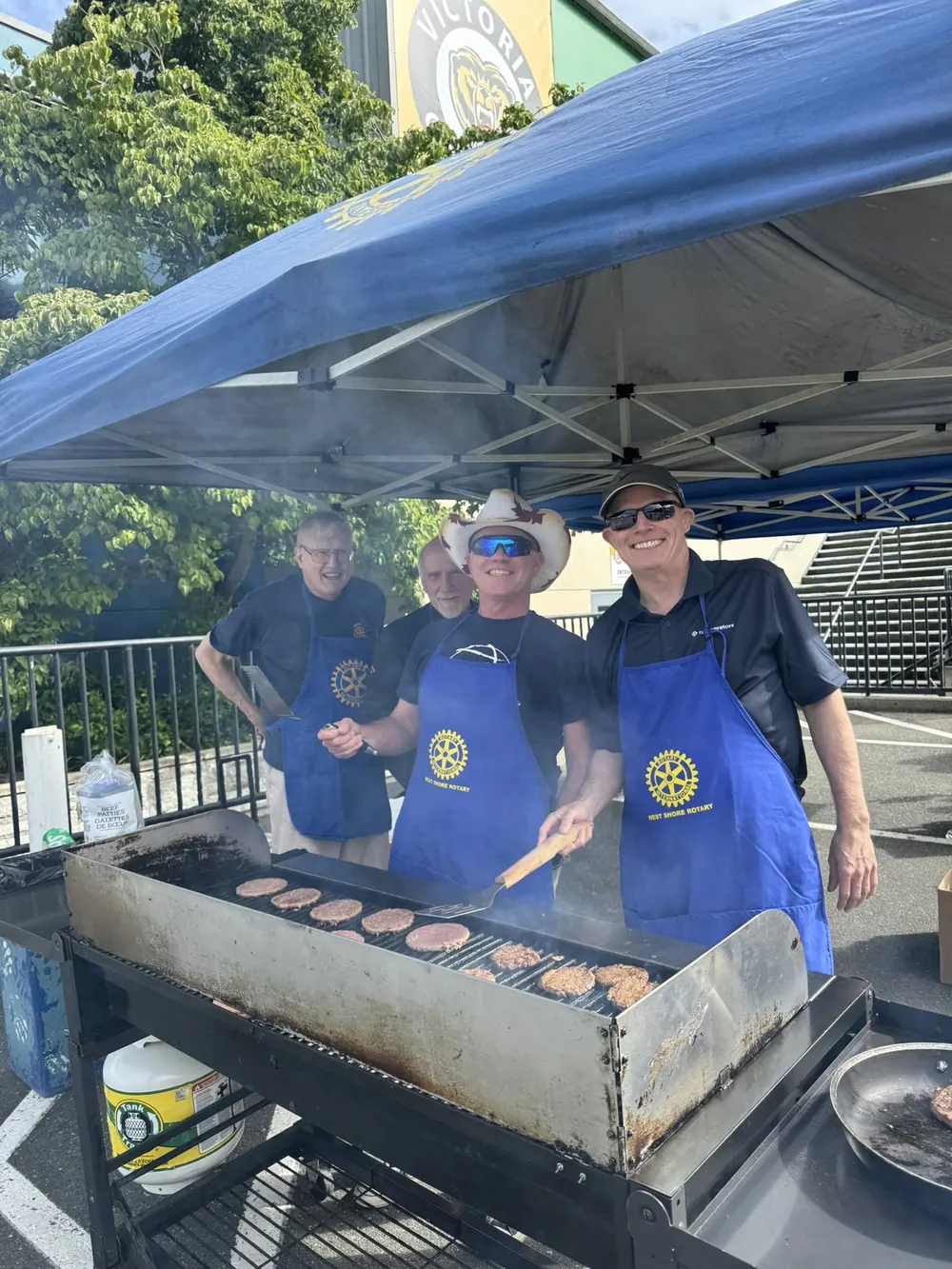Rotary members in West Shore Rotary aprons grilling burgers under a Rotary tent