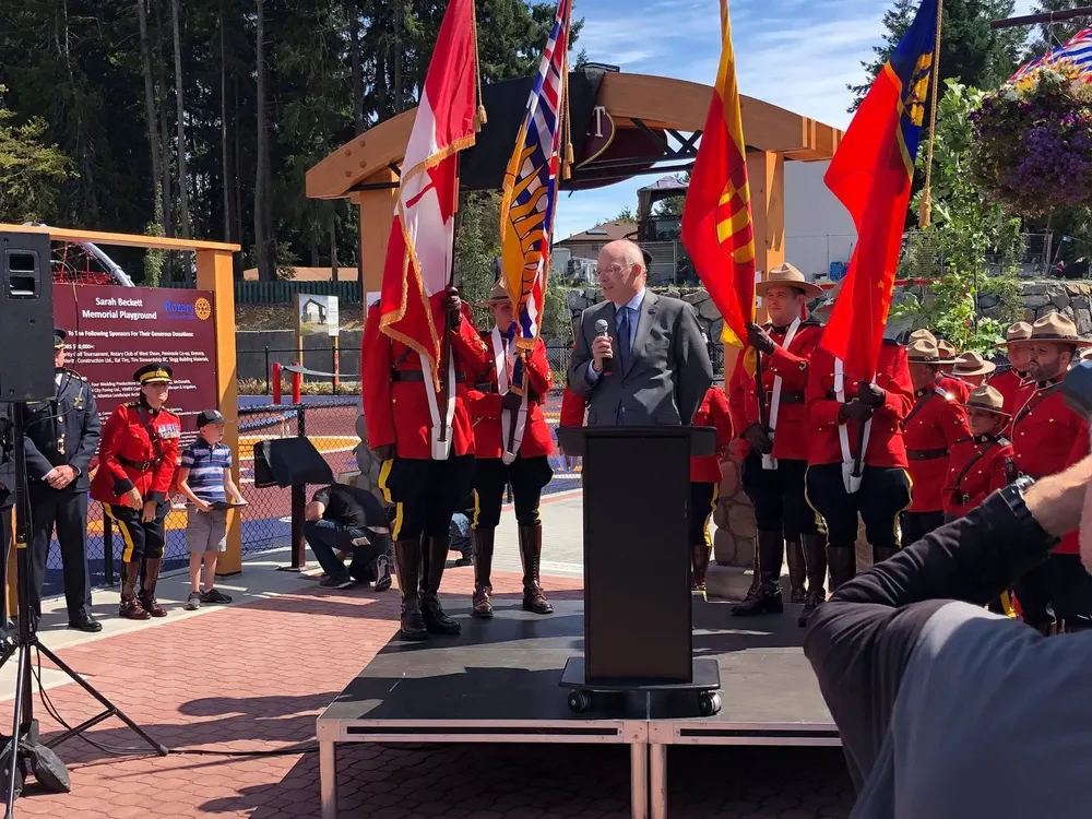 RCMP members in red serge with flags at the opening ceremony of the Sarah Beckett Memorial Playground